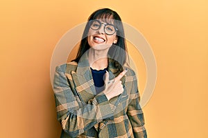 Young hispanic woman wearing business style and glasses smiling cheerful pointing with hand and finger up to the side