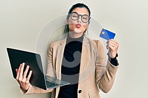 Young hispanic woman wearing business style holding laptop and credit card looking at the camera blowing a kiss being lovely and