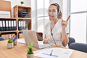 Young hispanic woman wearing call center agent headset at the office smiling happy pointing with hand and finger to the side