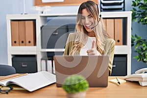 Young hispanic woman wearing call center agent headset working at the office smiling happy and positive, thumb up doing excellent