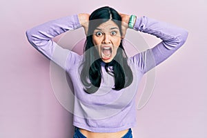 Young hispanic woman wearing casual clothes crazy and scared with hands on head, afraid and surprised of shock with open mouth