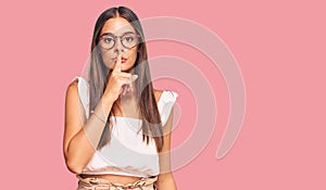 Young hispanic woman wearing casual clothes and glasses asking to be quiet with finger on lips