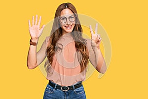 Young hispanic woman wearing casual clothes and glasses showing and pointing up with fingers number seven while smiling confident