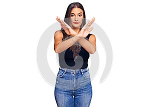 Young hispanic woman wearing casual clothes rejection expression crossing arms and palms doing negative sign, angry face