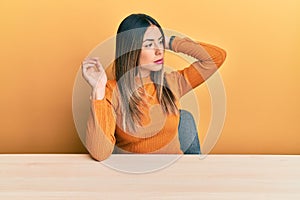 Young hispanic woman wearing casual clothes sitting on the table confuse and wondering about question