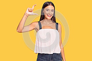 Young hispanic woman wearing casual clothes smiling and confident gesturing with hand doing small size sign with fingers looking