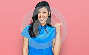 Young hispanic woman wearing casual clothes smiling with happy face looking and pointing to the side with thumb up
