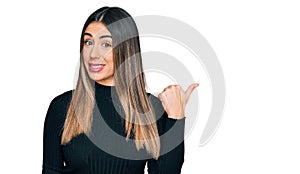 Young hispanic woman wearing casual clothes smiling with happy face looking and pointing to the side with thumb up