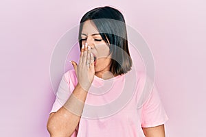 Young hispanic woman wearing casual pink t shirt bored yawning tired covering mouth with hand