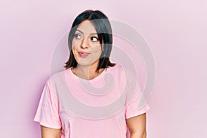 Young hispanic woman wearing casual pink t shirt smiling looking to the side and staring away thinking