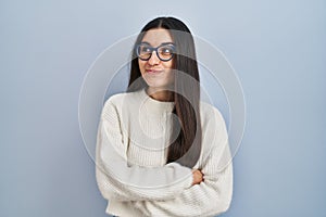 Young hispanic woman wearing casual sweater over blue background smiling looking to the side and staring away thinking