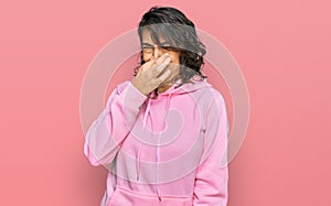 Young hispanic woman wearing casual sweatshirt smelling something stinky and disgusting, intolerable smell, holding breath with