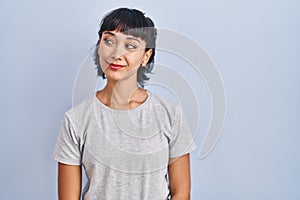 Young hispanic woman wearing casual t shirt over blue background smiling looking to the side and staring away thinking