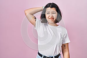 Young hispanic woman wearing casual white t shirt over pink background confuse and wondering about question