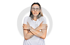 Young hispanic woman wearing casual white t shirt shaking and freezing for winter cold with sad and shock expression on face