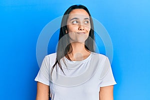 Young hispanic woman wearing casual white t shirt smiling looking to the side and staring away thinking