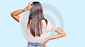 Young hispanic woman wearing casual white tshirt backwards thinking about doubt with hand on head
