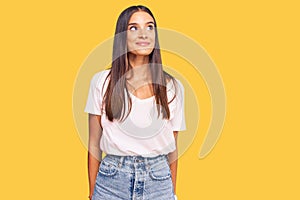 Young hispanic woman wearing casual white tshirt smiling looking to the side and staring away thinking