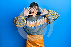 Young hispanic woman wearing casual winter sweater showing and pointing up with fingers number seven while smiling confident and