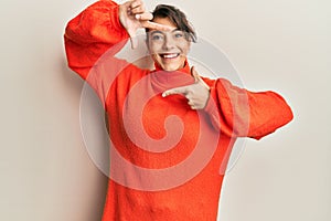 Young hispanic woman wearing casual winter sweater smiling making frame with hands and fingers with happy face