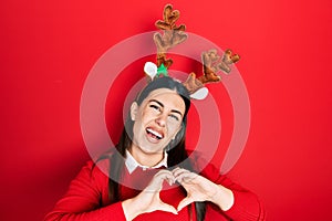 Young hispanic woman wearing cute christmas reindeer horns smiling in love showing heart symbol and shape with hands