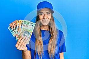 Young hispanic woman wearing delivery uniform and cap holding australian dollars looking positive and happy standing and smiling