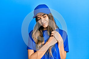 Young hispanic woman wearing delivery uniform and cap smiling with hands on chest with closed eyes and grateful gesture on face