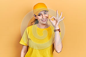 Young hispanic woman wearing delivery uniform and cap smiling positive doing ok sign with hand and fingers