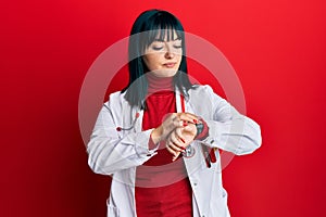 Young hispanic woman wearing doctor uniform and stethoscope checking the time on wrist watch, relaxed and confident