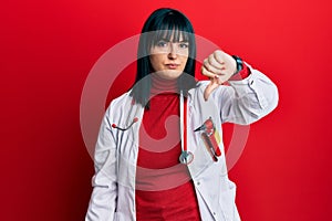 Young hispanic woman wearing doctor uniform and stethoscope looking unhappy and angry showing rejection and negative with thumbs