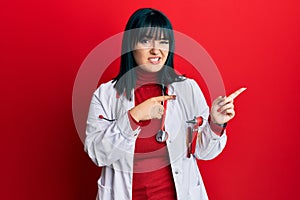 Young hispanic woman wearing doctor uniform and stethoscope pointing aside worried and nervous with both hands, concerned and