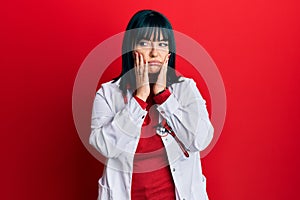 Young hispanic woman wearing doctor uniform and stethoscope tired hands covering face, depression and sadness, upset and irritated