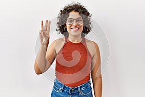 Young hispanic woman wearing glasses standing over isolated background showing and pointing up with fingers number three while