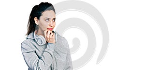 Young hispanic woman wearing gym clothes and using headphones thinking concentrated about doubt with finger on chin and looking up