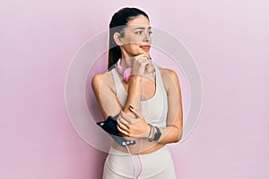 Young hispanic woman wearing gym clothes and using headphones thinking worried about a question, concerned and nervous with hand