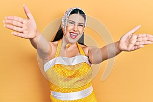 Young hispanic woman wearing pin up style looking at the camera smiling with open arms for hug