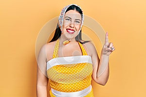 Young hispanic woman wearing pin up style smiling with an idea or question pointing finger up with happy face, number one