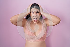 Young hispanic woman wearing pink bra crazy and scared with hands on head, afraid and surprised of shock with open mouth