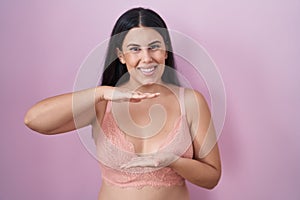 Young hispanic woman wearing pink bra gesturing with hands showing big and large size sign, measure symbol