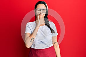 Young hispanic woman wearing professional waitress apron touching mouth with hand with painful expression because of toothache or