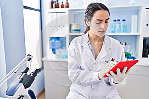 Young hispanic woman wearing scientist uniform using touchpad at laboratory