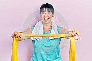 Young hispanic woman wearing sportswear and arm band sticking tongue out happy with funny expression