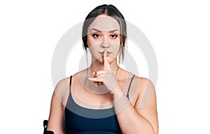 Young hispanic woman wearing sportswear asking to be quiet with finger on lips