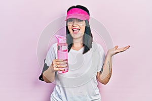 Young hispanic woman wearing sportswear drinking bottle of water celebrating achievement with happy smile and winner expression