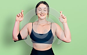 Young hispanic woman wearing sportswear gesturing finger crossed smiling with hope and eyes closed