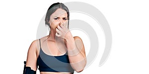Young hispanic woman wearing sportswear smelling something stinky and disgusting, intolerable smell, holding breath with fingers