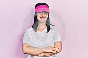 Young hispanic woman wearing sportswear and sun visor cap happy face smiling with crossed arms looking at the camera