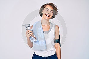 Young hispanic woman wearing sportswear and towel drinking bottle of water looking positive and happy standing and smiling with a