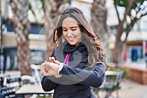 Young hispanic woman wearing sportswear using stopwatch at street