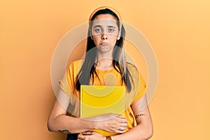 Young hispanic woman wearing student backpack and holding book depressed and worry for distress, crying angry and afraid